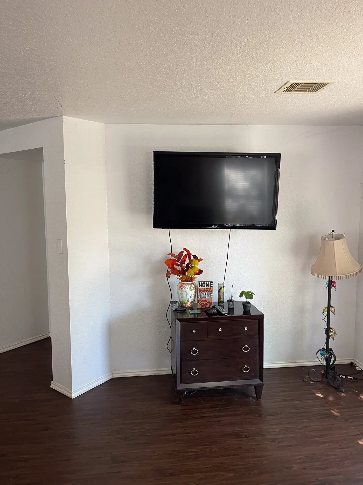 Living room corner with a wall-mounted television above a wooden chest.