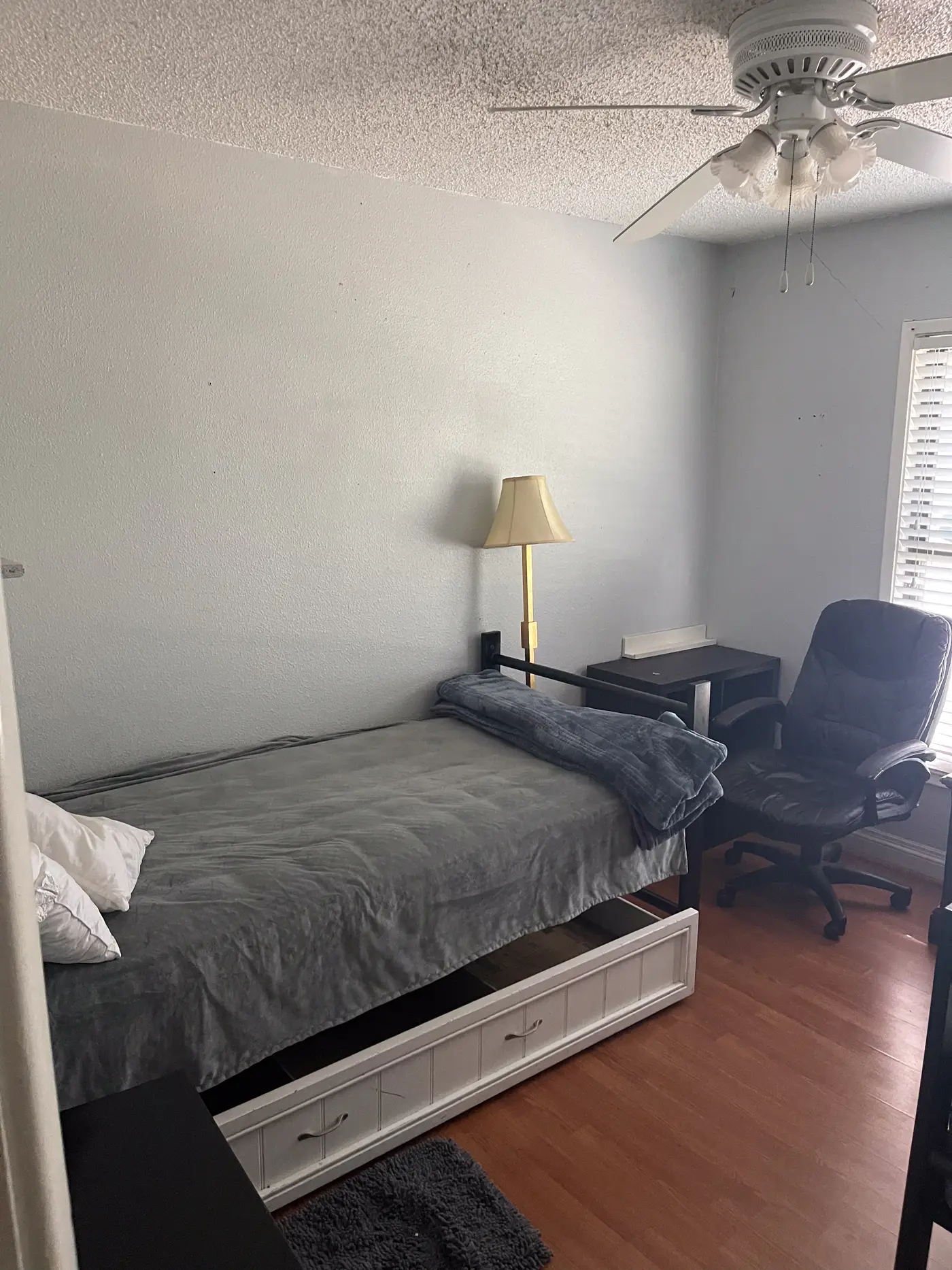 Bedroom with a bed, desk chair and wood flooring.