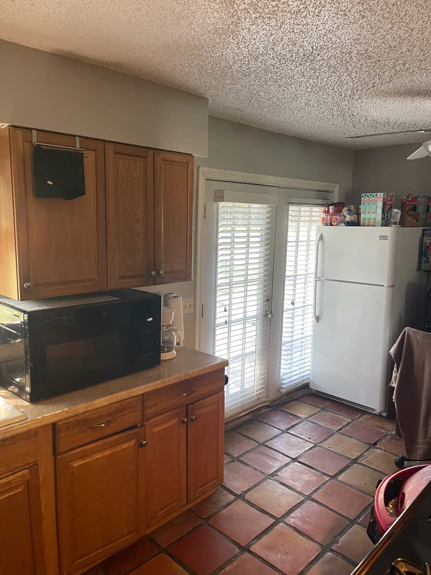Kitchen with wood cabinets, a microwave and tiled flooring.