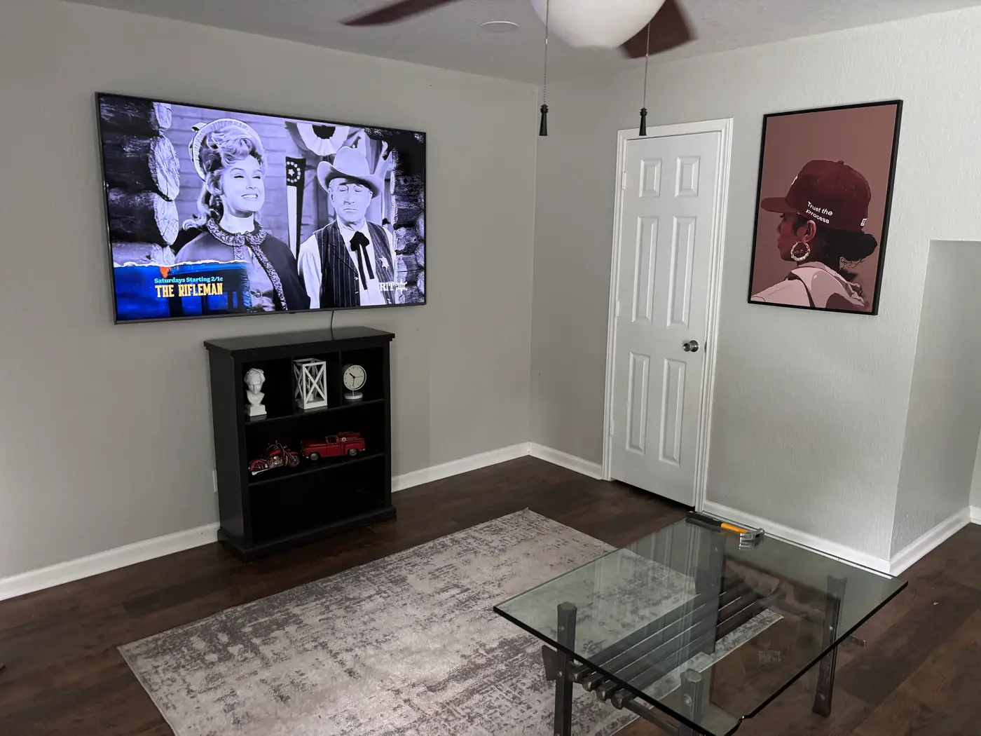 Living room with a wall-mounted television, dark bookcase and glass coffee table.