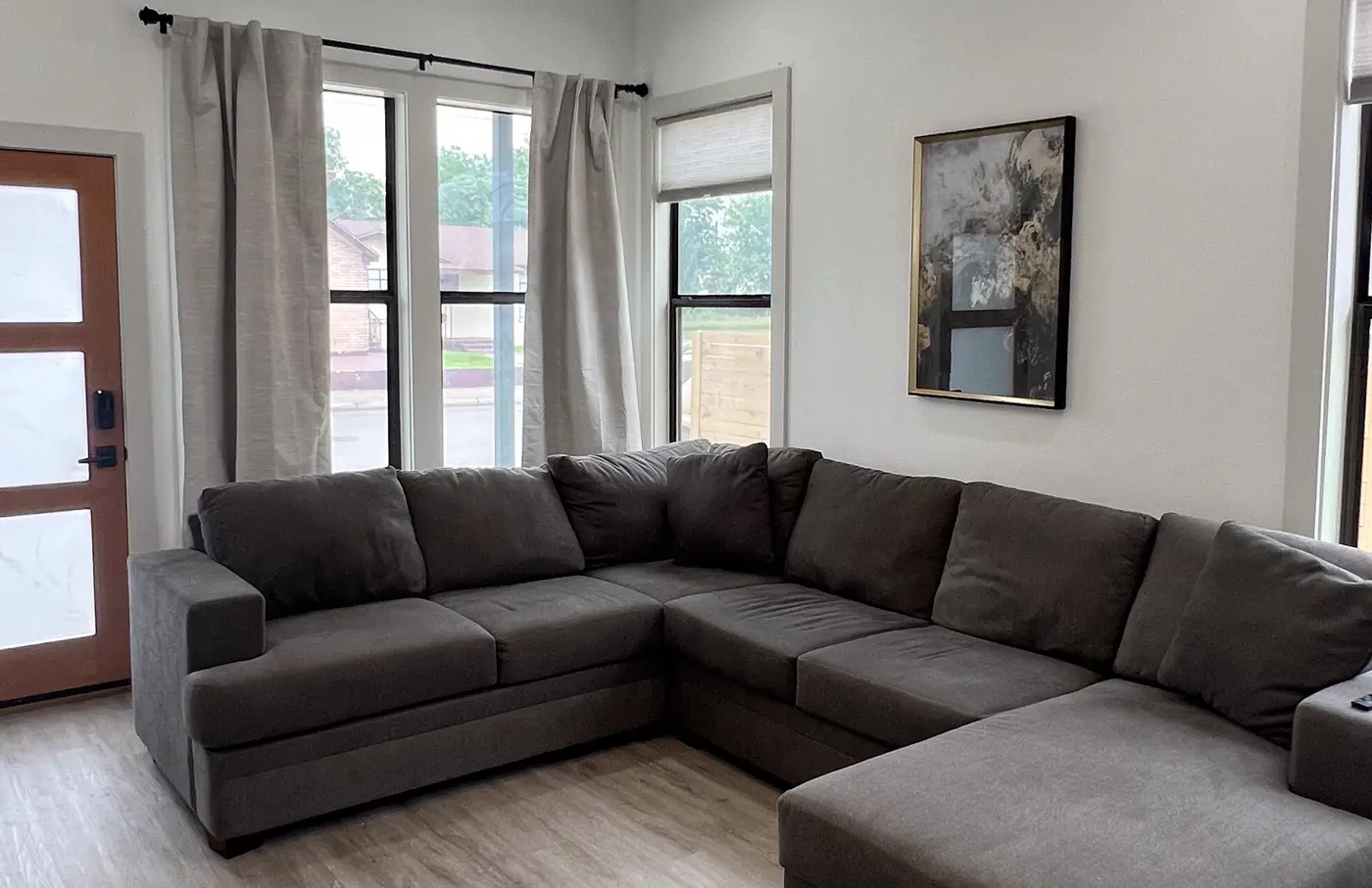 Living room with a gray sectional and framed prints, looking toward the front door.