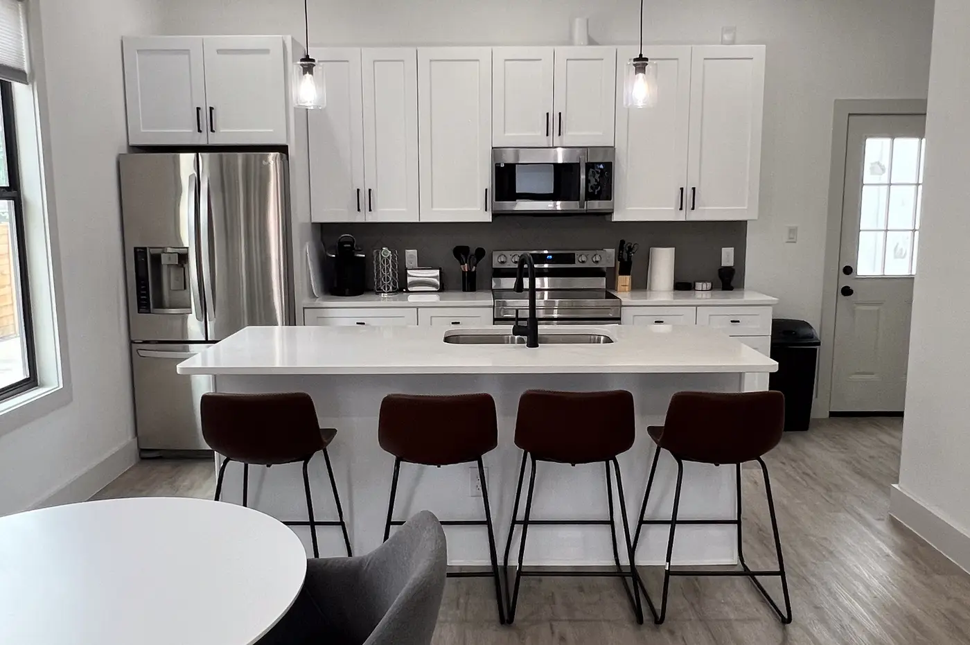 Kitchen island with four leather bar stools under pendant lights.