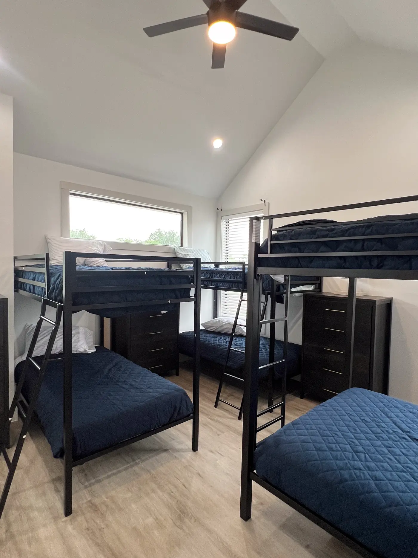 Bunk room with three bunk beds in navy bedding on light wood flooring.