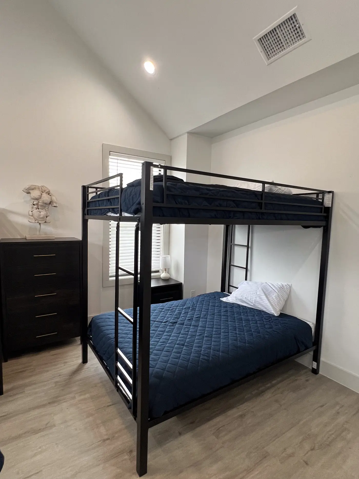 Bunk bed in navy bedding beside a dark dresser, lit by a window.