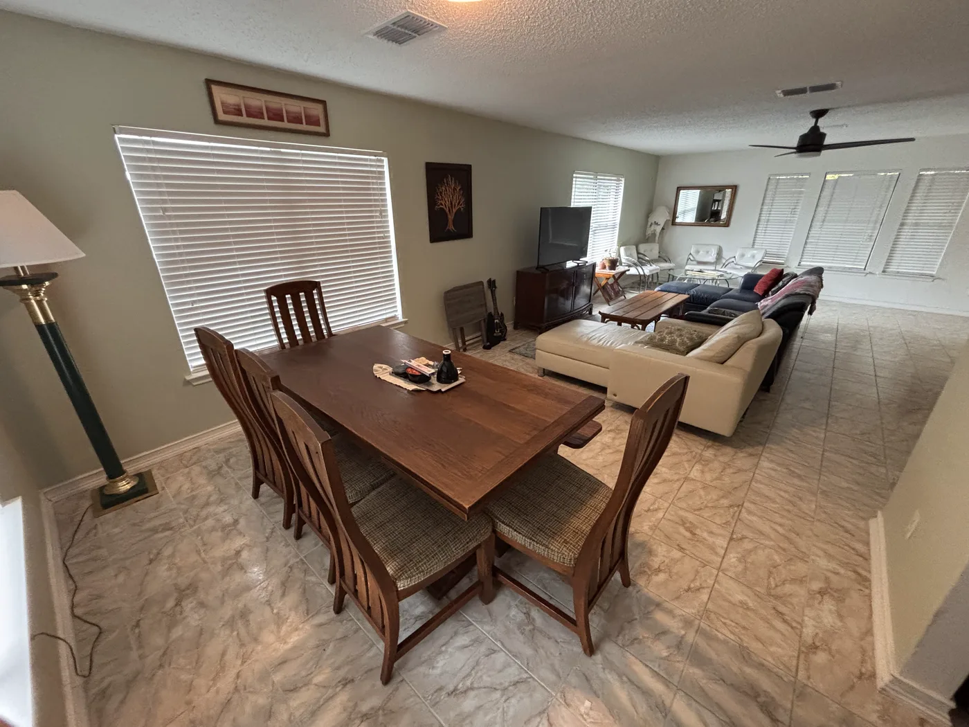 Dining table and six chairs beside a shuttered window, looking through to the living room.