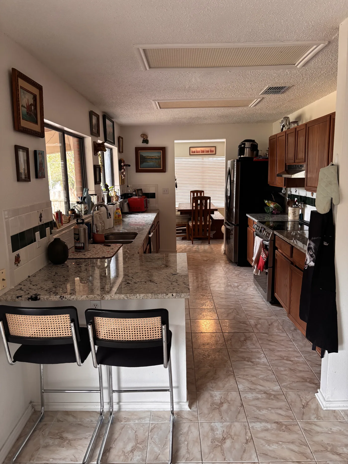 Kitchen breakfast bar with two cane stools and the dining nook beyond.