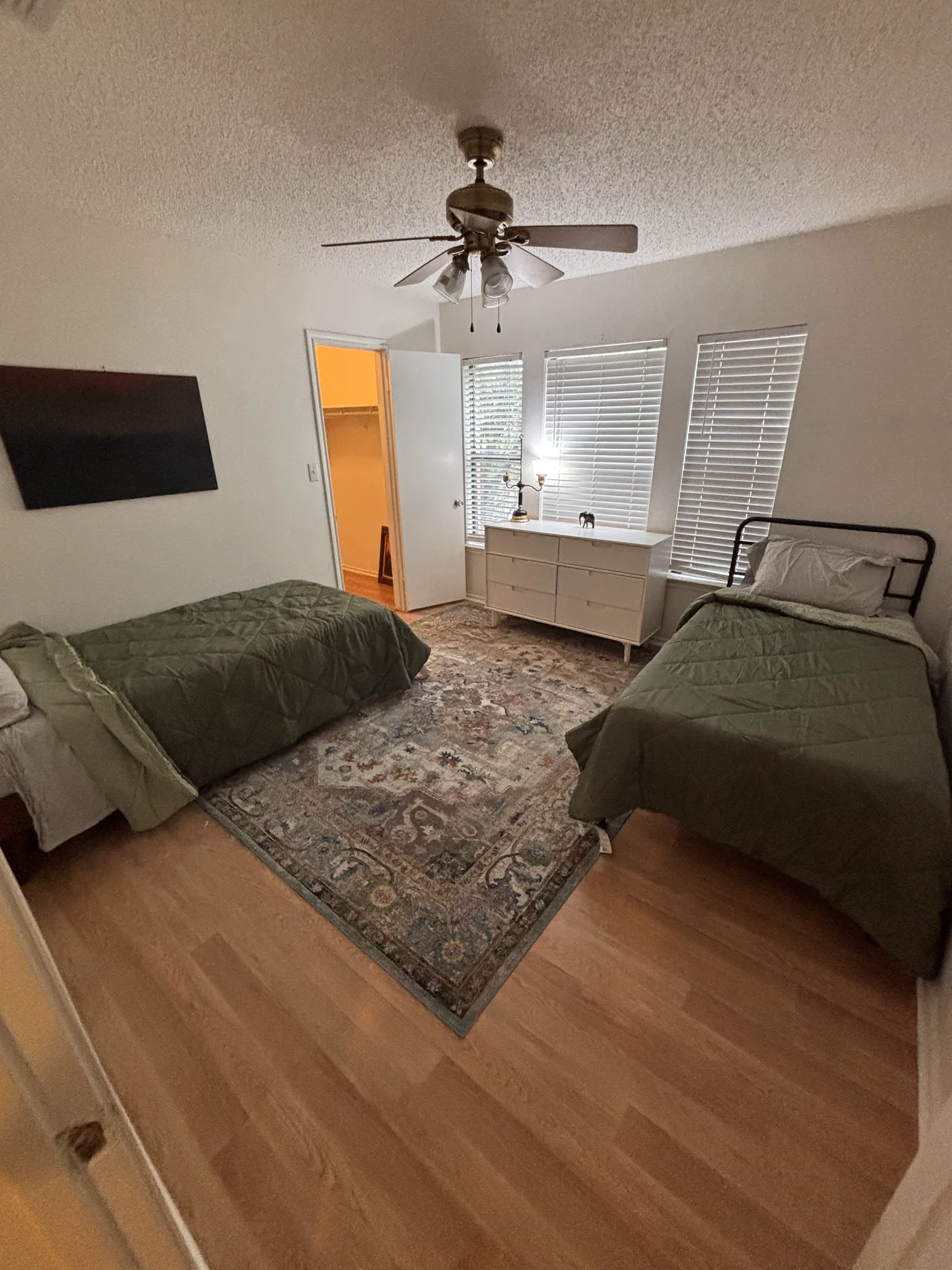 Bedroom with two beds either side of a patterned rug and a white dresser between the windows.