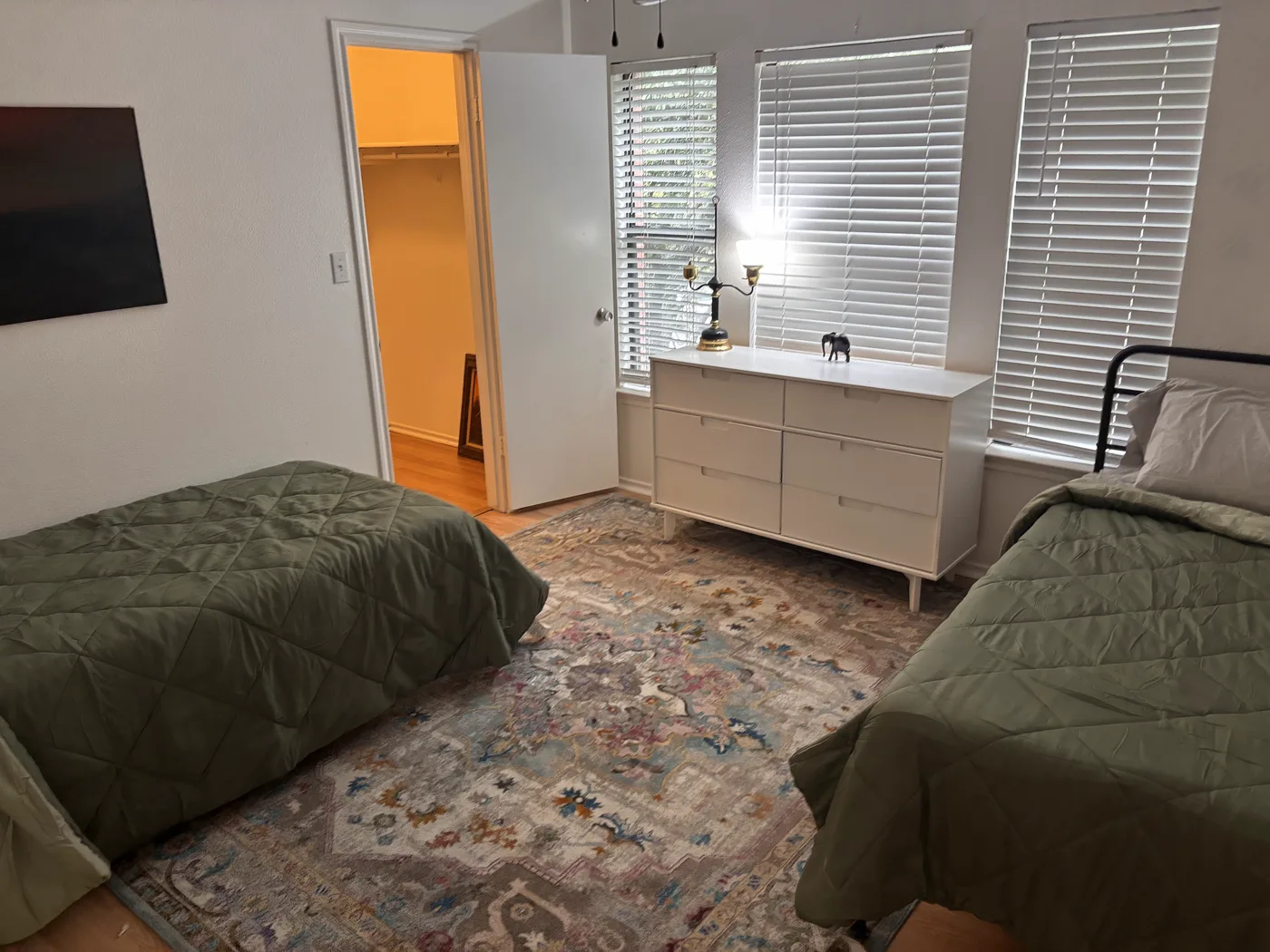 White six-drawer dresser under three shuttered windows in the two-bed room.