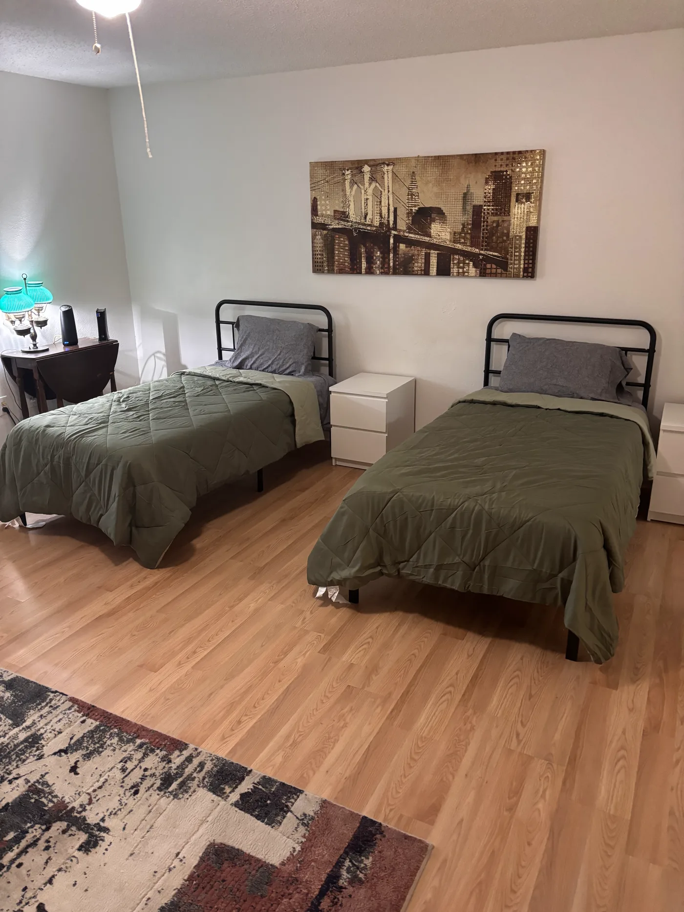 Two of the three beds in the large room, under a canvas print of a city skyline.