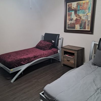 Two-man suite sober living bedroom in Austin with twin beds, artwork, and wood nightstand