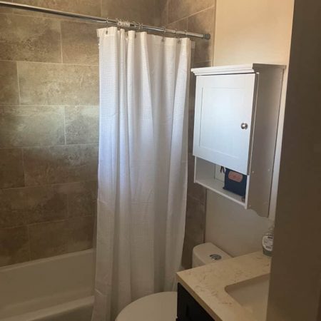 Clean bathroom in Austin sober living home with tiled shower, white curtain, and modern vanity