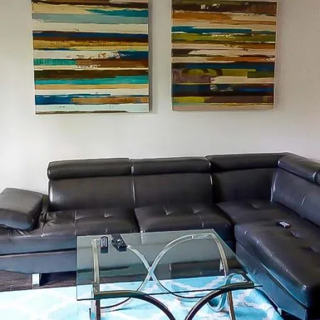 Cozy living area in Austin sober living home with sectional sofa, glass coffee table, and wall art